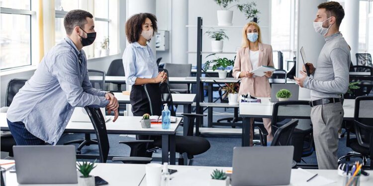 Modern team meeting, group work and social distancing. Manager with tablet speaks with workers in protective masks in interior of modern office with gadgets during coronavirus epidemic, free space