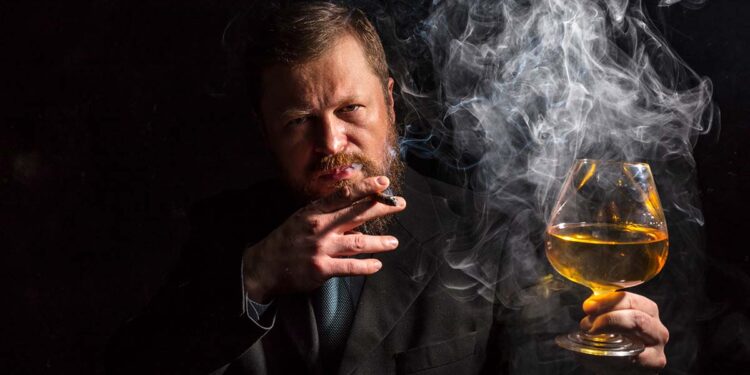 Solid confident bearded man in suit with glass of whisky and cigar with fume studio portrait