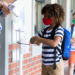 Multi ethnic group of school children wearing face masks, standing in line, having their temperature checked by a teacher. Education back to school health safety during Covid19 Coronavirus pandemic.