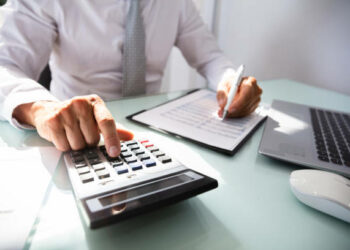 Close-up Of A Businessman's Hand Calculating Invoice With Calculator