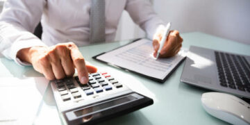 Close-up Of A Businessman's Hand Calculating Invoice With Calculator