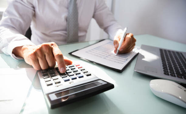 Close-up Of A Businessman's Hand Calculating Invoice With Calculator