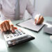 Close-up Of A Businessman's Hand Calculating Invoice With Calculator