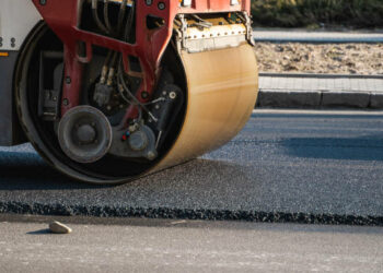 Asphalt road roller with heavy vibration roller compactor press new hot asphalt on the roadway on a road construction site. Heavy Vibration roller at asphalt pavement working. Repairing