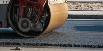 Asphalt road roller with heavy vibration roller compactor press new hot asphalt on the roadway on a road construction site. Heavy Vibration roller at asphalt pavement working. Repairing